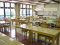 食堂の画像です。木製の机と椅子が並べられています。かなり広めの部屋です。
