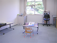 言語聴覚療法室の画像です。中央に机と椅子、奥にはパソコンが配置されています。明るい部屋です。